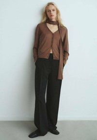 Brązowy sweter dzianinowy z dekoltem w serek i guzikami, w połączeniu z czarnymi spodniami o szerokich nogawkach. Stylizacja obejmuje pasujący szalik oraz płaskie buty.