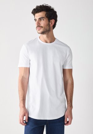 White cotton t-shirt with a round neckline and short sleeves, featuring a straight hem. Model is wearing blue jeans.