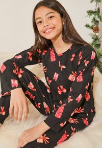 Set de pijamale negre cu motive de cadouri și fundițe roșii. Topul moale cu mâneci lungi se potrivește cu pantalonii asortați, creând un design coerent.