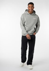 Light gray hooded sweatshirt with a front pocket and pink "Collective" logo, paired with black pants and white sneakers.