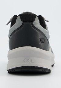 Basket de couleur noire et grise avec une tige texturée, un talon arrondi et une semelle intermédiaire blanche. Présente un logo sur le talon et des lacets pour un ajustement réglable.