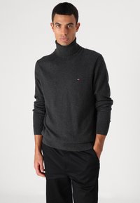 Maglione nero con collo alto in tessuto morbido, caratterizzato da un logo sottile sul petto e polsini e orlo a coste.