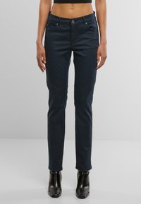 Jeans azul marino con un ajusteSlim, diseño de cinco bolsillos, cierre de botón metálico y un ligero estiramiento. Combinados con botines negros de tacón alto.