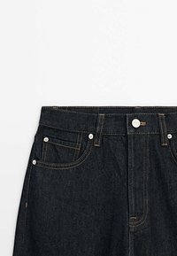 Mörka denimjeans med fem fickor, kontrasterande gul sömnad, metallnitar och knappstängning fram.