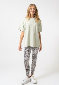 Svetle zelené oversized tričko s nápisem "OH DUBEN", doplněné šedými legínami se zvířecím potiskem a bílými platformovými teniskami. Hladká textilie.