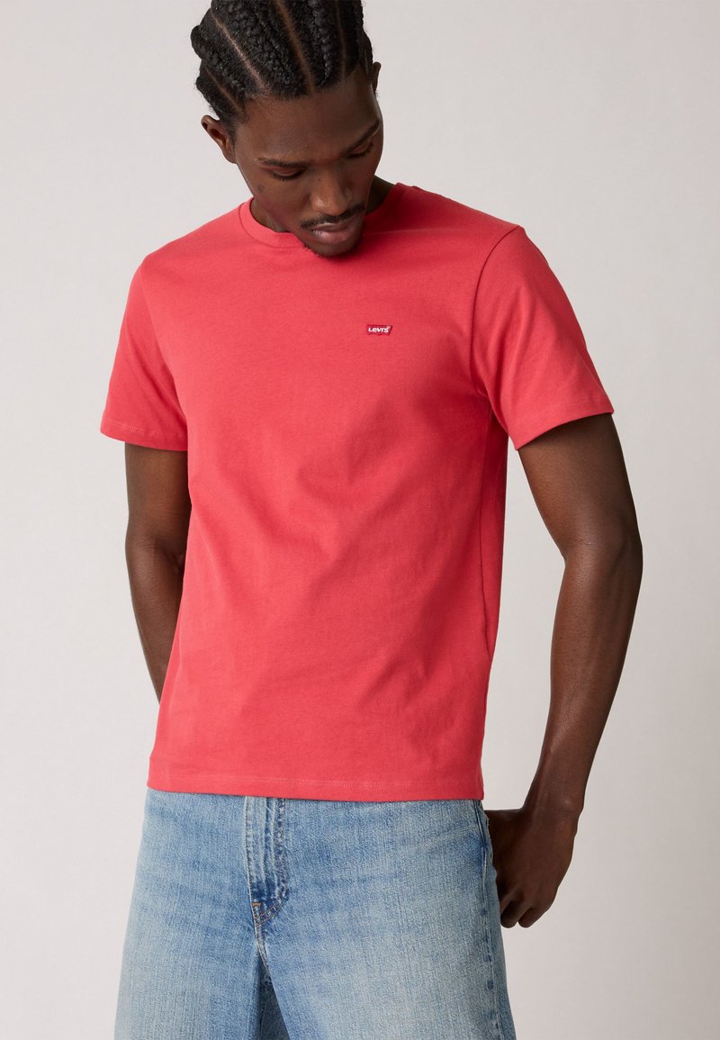 T-shirt en coton rouge avec un col rond, des manches courtes et un petit logo Levi's sur la poitrine. Associée à un jean en denim bleu clair.