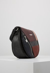 Kulatá křížová taška v černé, tmavě červené a šedé kůži. Obsahuje zipové uzavření, pletený okraj a plochý ramenní popruh.