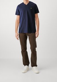 Námornická v-neck tričko vyrobené z bavlny, spárované s hnědými kordovými kalhotami a bílými teniskami; má malou zelenou značku na hrudi.