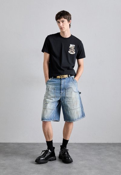 Svart t-skjorte med grafisk trykk, blå gaten shorts med falmede områder, og klumpete svarte sko, komplementert med et gult belte.