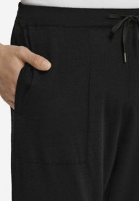 Czarne dresy z miękkiego materiału, z elastycznym pasem na sznurek, bocznymi kieszeniami i gładką teksturą. Zbliżenie na obszar bioder.