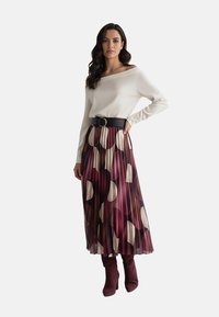 Biała bluzka odkrywająca ramiona, czarny pasek w talii i plisowana spódnica z dużymi fioletowo-kremowymi okrągłymi wzorami. Bordowe kozaki za kolano.