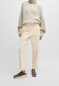 Pull en maille beige avec un motif torsadé texturé, associé à un pantalon large crème et des baskets marron avec une tige texturée et une semelle blanche.