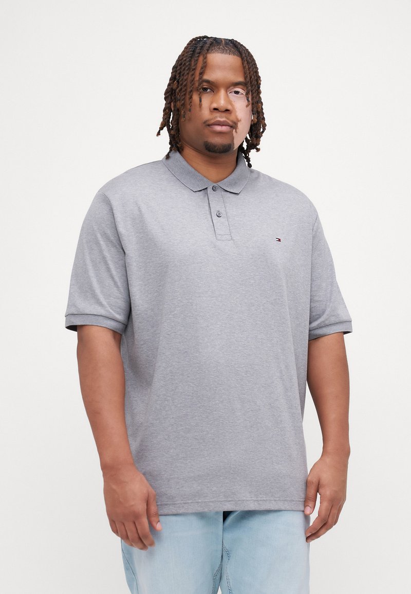 Polo grigio con colletto e bottoni, maniche corte, vestibilità rilassata, con un piccolo logo sul petto, indossato con jeans azzurri chiari.