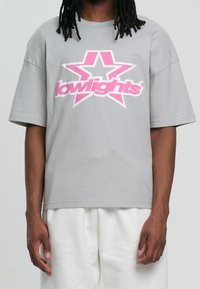 Camiseta gris de gran tamaño con un gran gráfico de estrella rosa y el texto "lowlights" en letras negritas. Material de algodón suave, corte relajado.