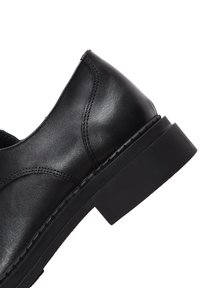 Schwarzer Lederschuh mit glatter Oberfläche, runder Spitze, niedrigem Blockabsatz und dezenten Nahtdetails an den Seiten.