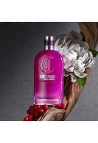 Rosa glassparfymeflaske med rund form, sølvhette og preget logo. Omgitt av røde bær og en teksturert tregren.