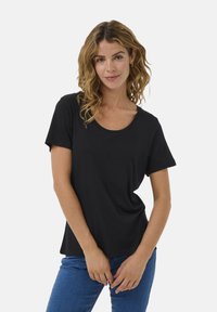 Čierne tričko s krátkym rukávom a okrúhlym výstrihom, vyrobené z mäkkej tkaniny. V kombinácii s modrými džínami, ktoré majú uvoľnený strih.