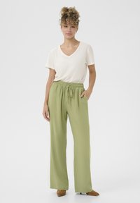 Lätt, krämfärgad t-shirt med V-hals som är kombinerad med löst sittande, olivgröna byxor med elastisk midja och sidofickor. Mockaskor i tan-färg.