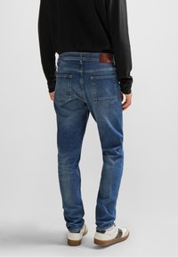 Jeans i denim i medelblå färg med en lätt blekhet. Standard femficksdesign, rak benpassform och ett brunt läderlogopatch på midjan.