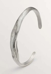 Brazalete de plata en forma de puño con una superficie ondulada y texturizada que se asemeja a la veta de la madera. Los extremos curvados y elegantes realzan el diseño orgánico.