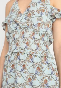 Ljusblå klänning med blommönster, volangärmar, smockad bodice och lager av fräser. Mjuk tygkvalitet framhäver designdetaljerna.