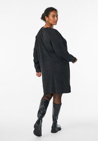 Robe en tricot noir à manches longues, coupe décontractée, et col en dentelle, associée à des bottes noires brillantes jusqu'aux genoux.