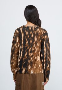 Knit sweater featuring a brown and black abstract pattern, ribbed neckline, and long sleeves, with a relaxed fit and textured finish.