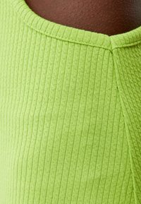 Tessuto a coste, di un verde brillante, con una finitura testurizzata. Collo rotondo con bordi cuciti a contrasto. Nessun hardware o motivo visibile.