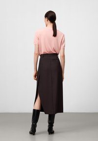 Lichtroze T-shirt met korte mouwen, gecombineerd met een donkerbruine hoge taille rok met een zijsplitting en een achterzak. Zwarte kniehoge laarzen.
