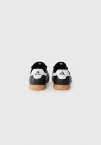 Black and white athletic shoes with a textured finish, gum rubber sole, and three stripes design. Heel features an Adidas logo detail.