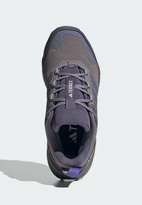 Scarpa da ginnastica grigia con tomaia in rete, suola di gomma e accenti violacei tenui. Presenta una punta rinforzata e un sistema di lacci sicuro.