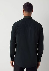 Camicia a maniche lunghe verde scuro con colletto testurizzato e orlo dritto. Presenta polsini con bottoni e una finitura in tessuto liscia.