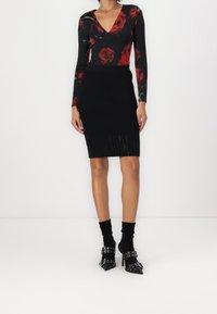 Bodysuit noir à manches longues avec imprimés de roses rouges, associé à une jupe noire côtelée jusqu'aux genoux et des chaussures noires à talons avec des accents de boucle.