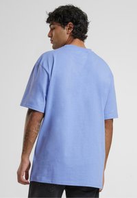 Light blue short-sleeve t-shirt made of cotton with a relaxed fit. Features a round neckline and back seam details, paired with dark pants.
