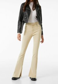 Beige utsvängda jeans med sidsprund, kombinerade med en svart läderjacka i kort modell och en åtsittande vit ribbad topp. Svarta plattformsskor.