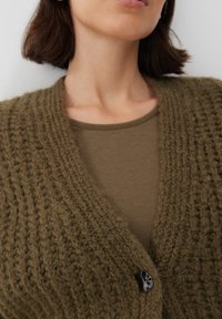 Stickad olivgrön cardigan med djup V-ringning, prydd med en framträdande svart knapp framtill och en mjuk, texturerad väv.