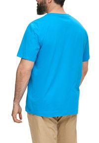 Turkusowy bawełniany t-shirt z krótkimi rękawami, prosty fason i klasyczny okrągły dekolt, noszony z beżowymi spodniami, przedstawiający prosty widok z tyłu.