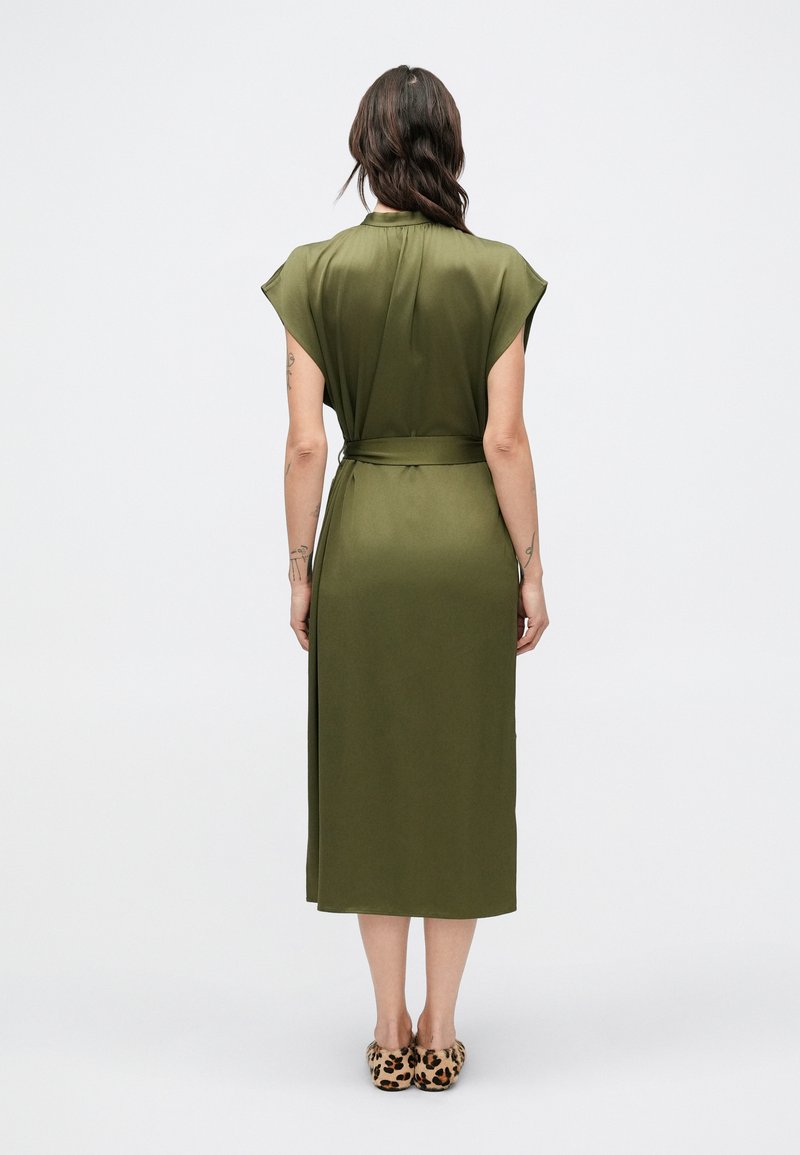 Olive green midi dress with short cap sleeves, tied waist detail, smooth texture, and a relaxed fit, paired with leopard print slippers.