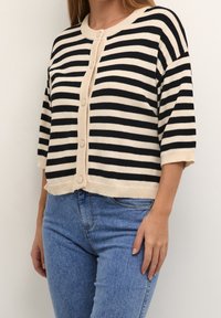 Gestreifter Cardigan mit kurzen Ärmeln, der schwarze und beige horizontale Streifen aufweist, einen gerippten Halsausschnitt hat und fünf Knöpfe an der Vorderseite besitzt.