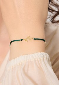 Zielona bransoletka z cordu z akcentem w postaci złotego liścia, charakteryzująca się eleganckim designem i gładką fakturą, zabezpieczona dekoracyjnymi węzłami.