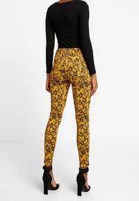 Leggings de estampado de serpiente amarillos con un diseño ajustado, que presentan una textura suave y acentos negros en el tobillo. Combinados con una blusa negra de canalé.