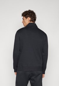 Sudadera negra con cuello alto, textura suave y puños acanalados. Diseñada con detalles mínimos y un corte holgado.