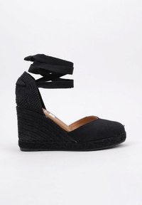 Zapato de cuña de esparteña negra con parte superior de tela, punta al aire y tiras cruzadas en el tobillo. El tacón de cuña envuelto en yute añade textura y altura.