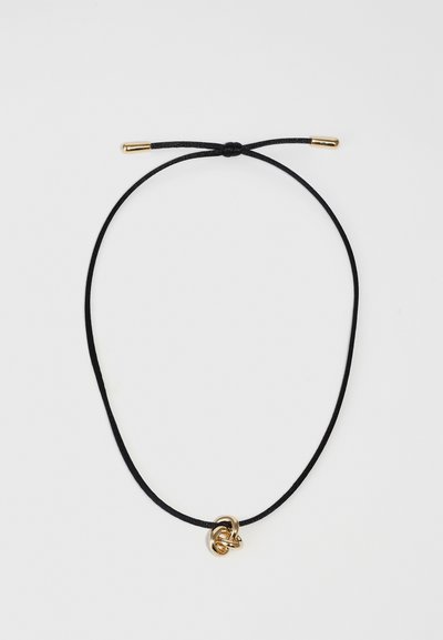 Un collier en cordon noir avec un pendentif en métal doré en forme de nœud. Le cordon est ajustable avec des extrémités en matériel doré et possède une texture lisse dans l'ensemble.