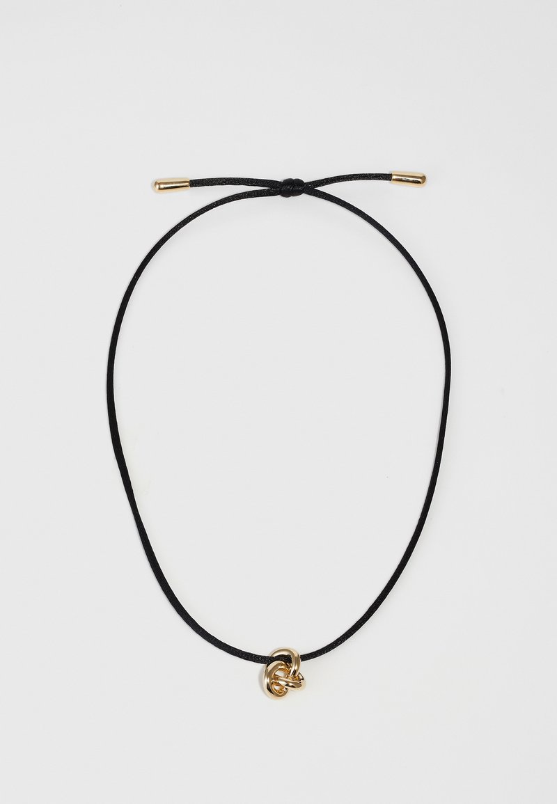 Juodos virvės kaklo papuošalas su auksinės spalvos metaliniu mazgo pakabuku. Virvė yra reguliuojama, su auksinėmis detalėmis, visuose paviršiuose sklandžiu tekstūru.