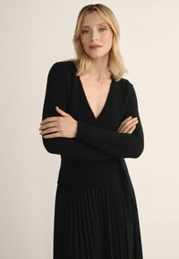 Czarny sweter typu v-neck wykonany z miękkiego materiału, z długimi rękawami i lekko dopasowanym krojem w połączeniu z czarną plisowaną spódnicą.