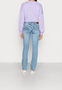 Light purple oversized sweatshirt paired with light blue jeans featuring decorative stitching on the back pockets. Casual footwear completes the look.