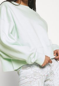 Mintgrön sweatshirt med sänkt axelparti, ribbade ärmslut och nederkant. Tyget verkar mjukt. Bärs med mönstrade metalliska leggings.