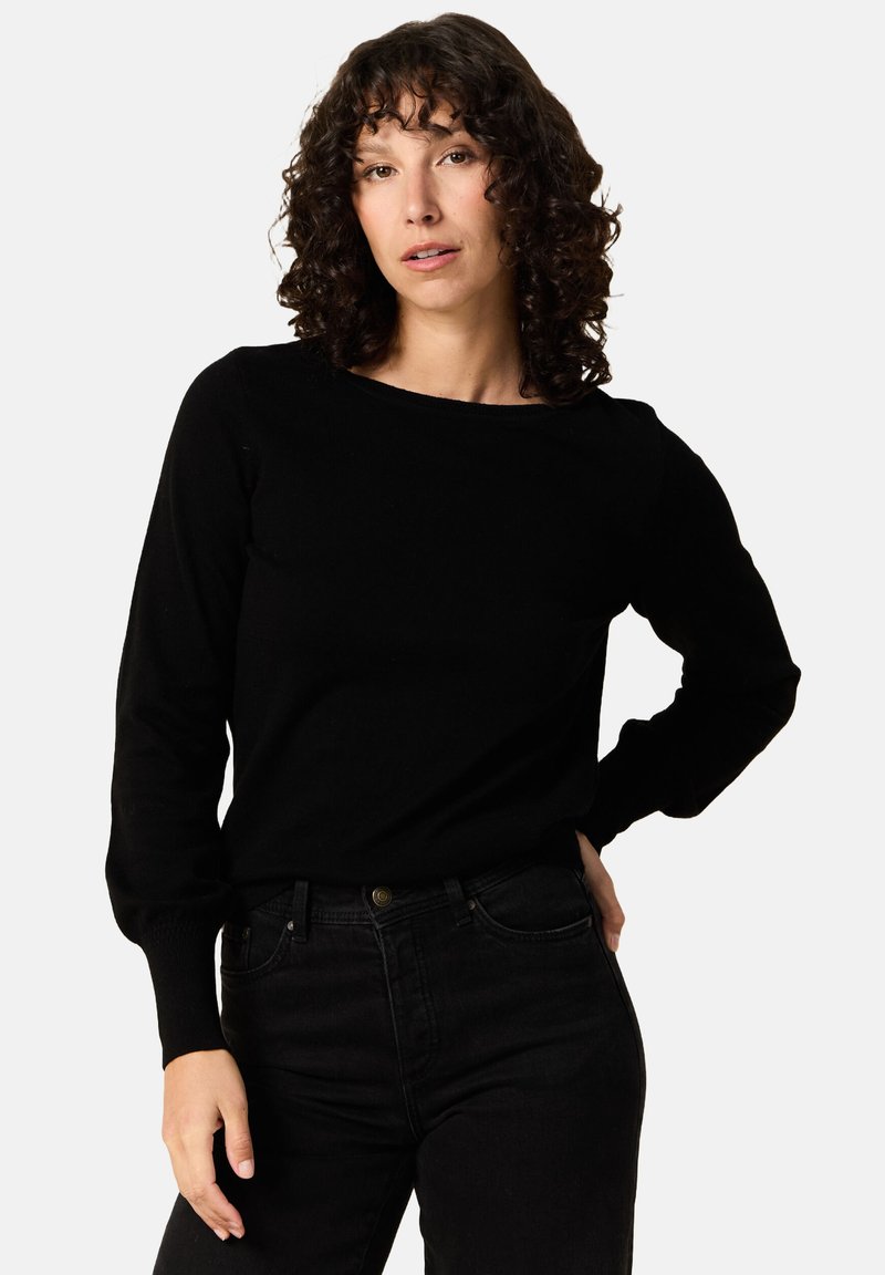 Musta pitkähihaiseksi neuleeksi, jossa on avara kaula-aukko ja istuvat hihansuut, valmistettu pehmeästä kankaasta, yhdistetty korkeavyötäröisten mustien farkkujen kanssa.