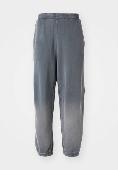 Pantaloni de jogging gri cu o textură moale, cu glezne înguste, buzunare laterale și un gradient subtil de la gri închis la gri mai deschis. Talie elastică în partea de sus.